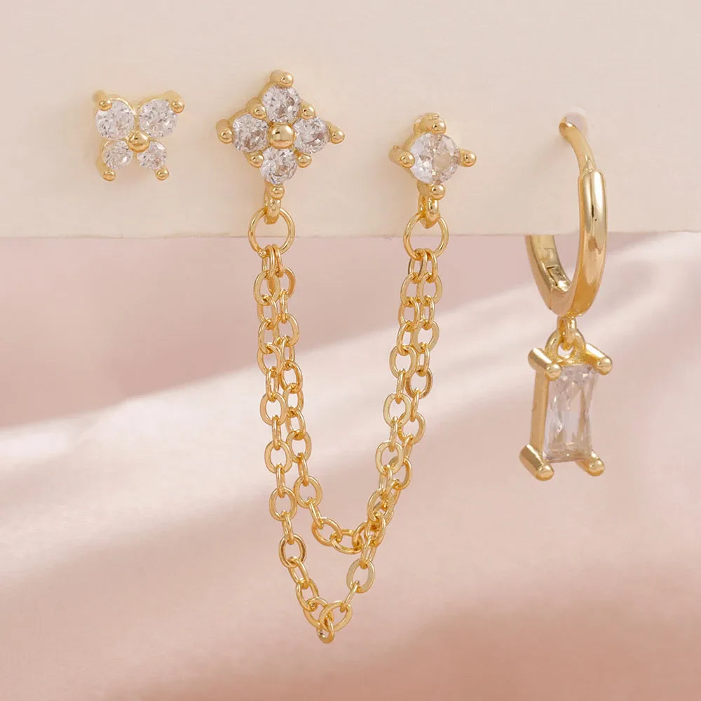 Set of gold earrings including chain, butterfly, and hoop designs on a soft pink background