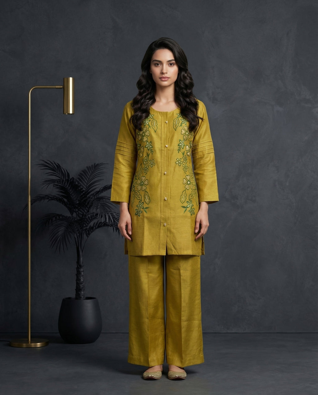 Woman wearing a mustard yellow embroidered outfit standing against a dark background with decorative elements.